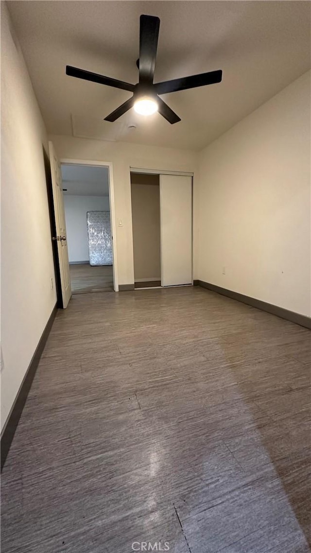 unfurnished bedroom featuring ceiling fan, baseboards, a closet, and wood finished floors