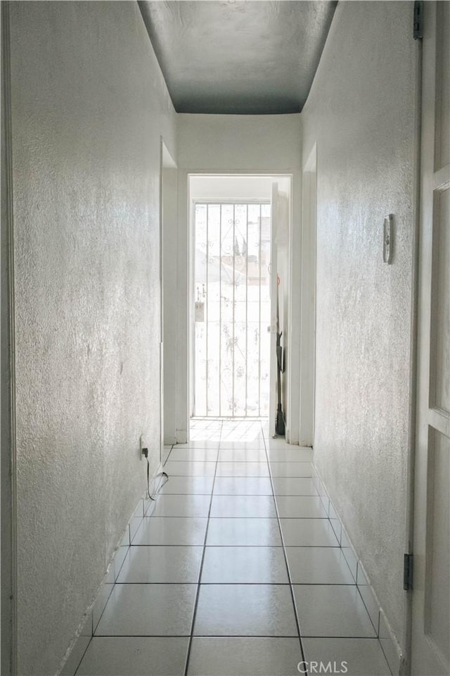 hallway with a textured wall and light tile patterned floors