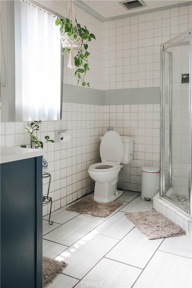 bathroom with a shower stall, tile patterned flooring, visible vents, toilet, and tile walls