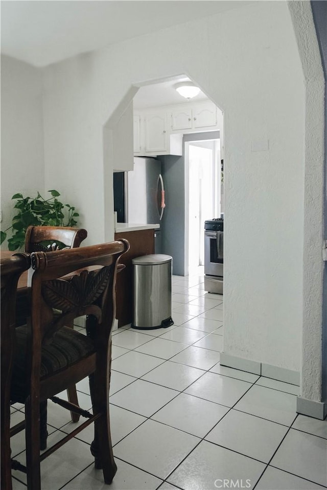 interior space featuring range, light tile patterned floors, white cabinetry, freestanding refrigerator, and arched walkways
