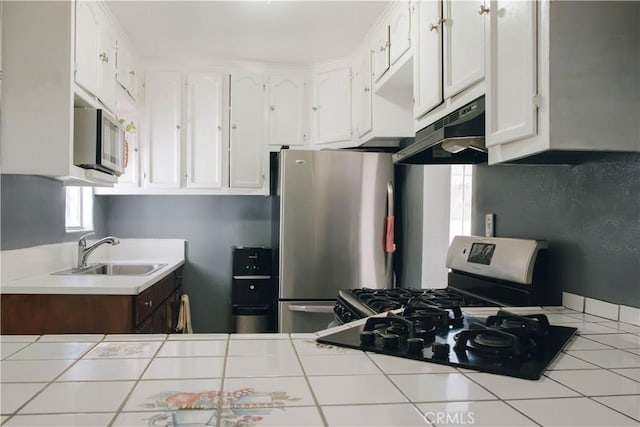 kitchen with white cabinets, under cabinet range hood, stainless steel appliances, tile countertops, and a sink