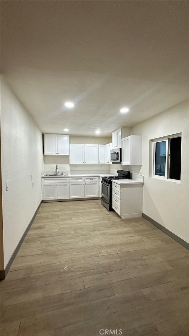 kitchen featuring white cabinets, baseboards, a sink, light wood-style floors, and stainless steel appliances