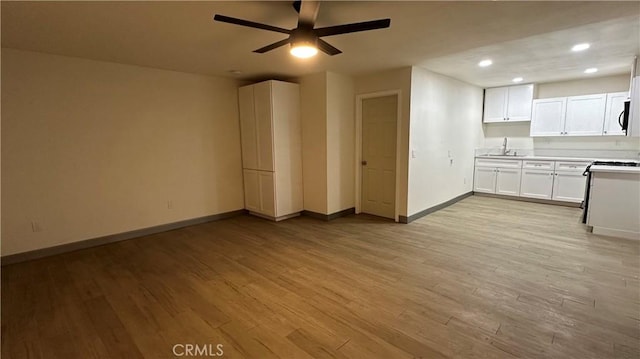 kitchen featuring baseboards, recessed lighting, light wood-style flooring, ceiling fan, and a sink