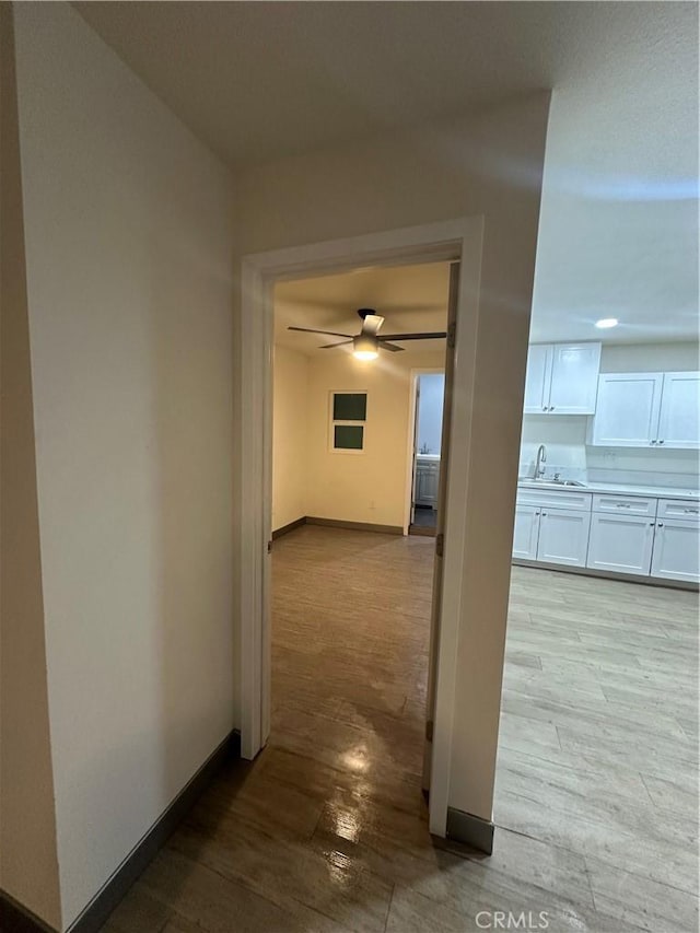 hall with a sink, light wood-style flooring, and baseboards