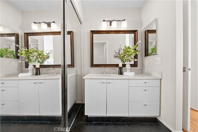 full bath with baseboards, two vanities, and a sink