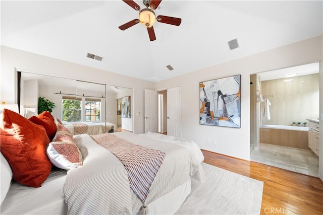 bedroom featuring light wood finished floors, visible vents, vaulted ceiling, and ensuite bathroom