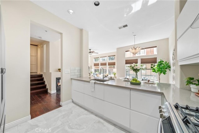 kitchen with visible vents, a glass covered fireplace, stainless steel range oven, white cabinetry, and a sink