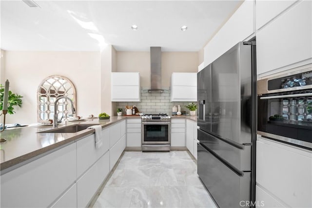 kitchen featuring tasteful backsplash, appliances with stainless steel finishes, white cabinets, a sink, and wall chimney range hood