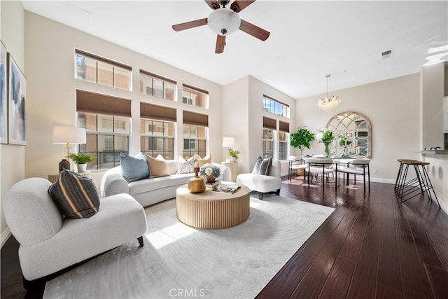 living room featuring wood-type flooring, visible vents, a towering ceiling, baseboards, and ceiling fan with notable chandelier