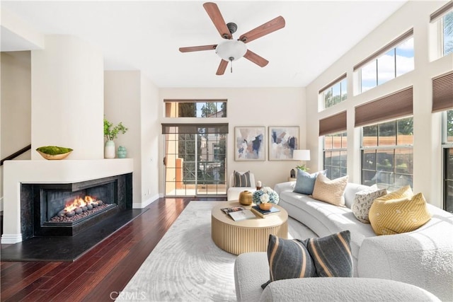 living room with a warm lit fireplace, baseboards, ceiling fan, and hardwood / wood-style floors