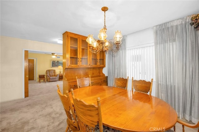 dining space with ceiling fan with notable chandelier and light colored carpet