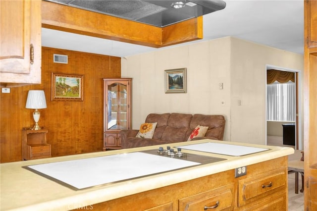 kitchen with brown cabinetry, wooden walls, visible vents, and light countertops