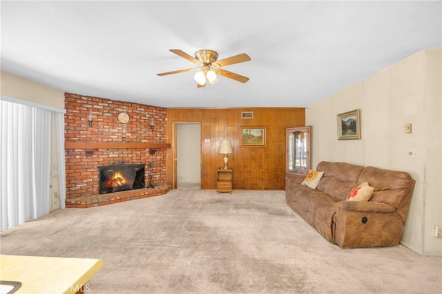 carpeted living room with wood walls, a fireplace, visible vents, and a ceiling fan