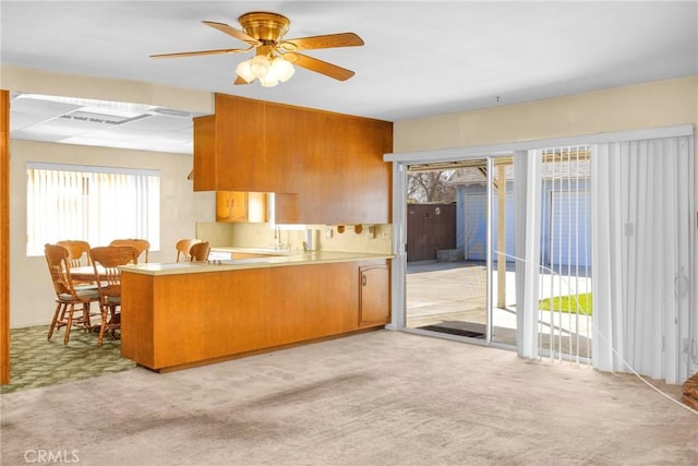 kitchen with light carpet, brown cabinetry, a peninsula, light countertops, and a sink