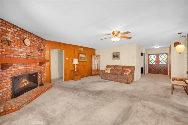 carpeted living room with visible vents, a fireplace, wooden walls, and ceiling fan