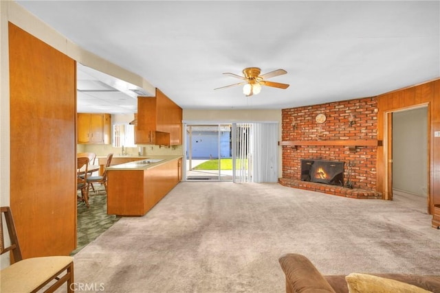 carpeted living room with a ceiling fan, a fireplace, wooden walls, and a sink