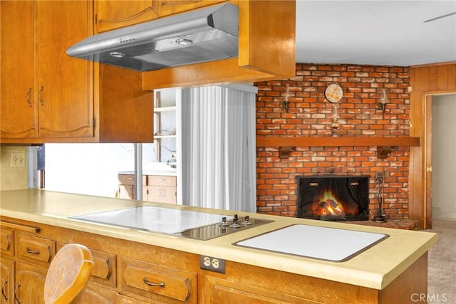 kitchen featuring brown cabinets, light countertops, a fireplace, and under cabinet range hood