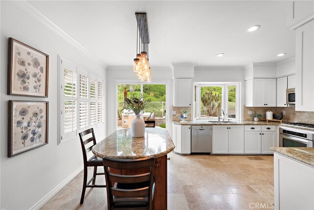 kitchen with light stone counters, stainless steel appliances, ornamental molding, decorative backsplash, and white cabinetry