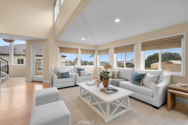 living area with recessed lighting, light wood-type flooring, baseboards, and a towering ceiling