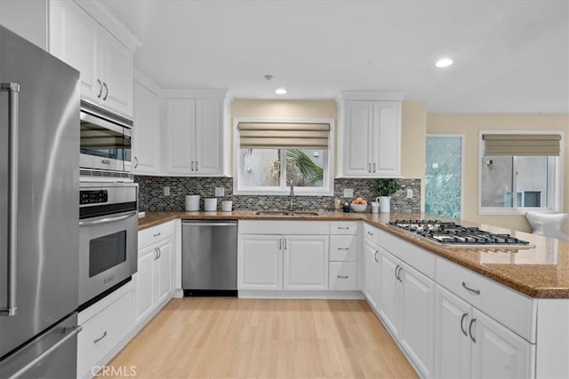 kitchen featuring stone counters, a sink, stainless steel appliances, light wood-style floors, and white cabinetry