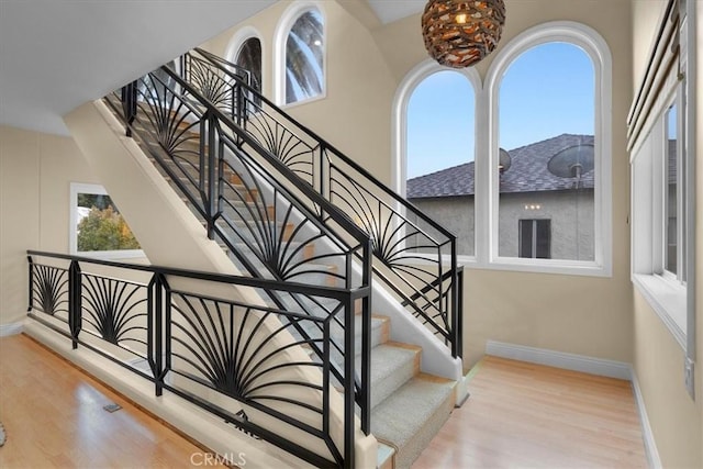 stairway featuring baseboards, a healthy amount of sunlight, and wood finished floors