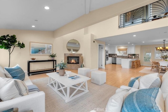 living area featuring light wood finished floors, recessed lighting, a high end fireplace, vaulted ceiling, and a notable chandelier