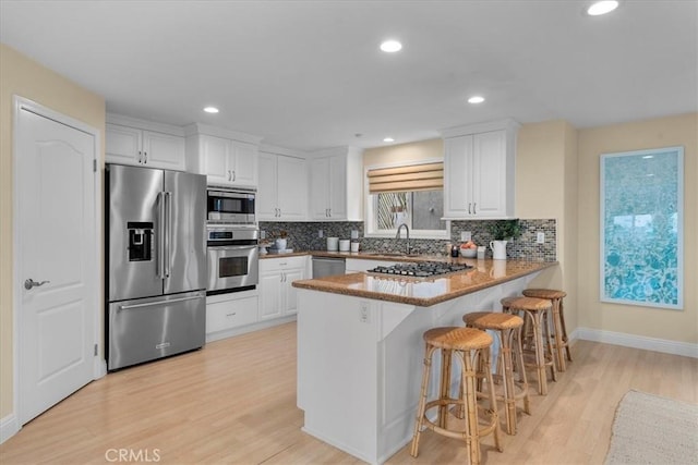 kitchen with light wood finished floors, a peninsula, white cabinets, stainless steel appliances, and a sink