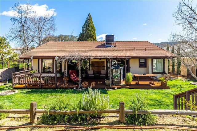 back of property featuring a tiled roof, fence, a deck, and a yard