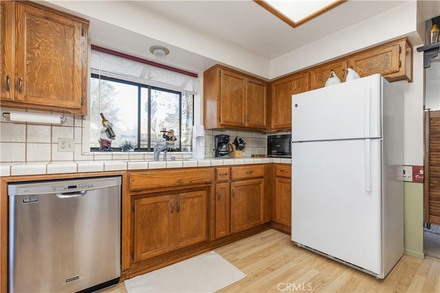 kitchen with light wood-style flooring, brown cabinets, freestanding refrigerator, decorative backsplash, and dishwasher