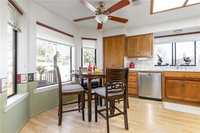 kitchen with tile counters, brown cabinetry, light wood-style flooring, and stainless steel dishwasher