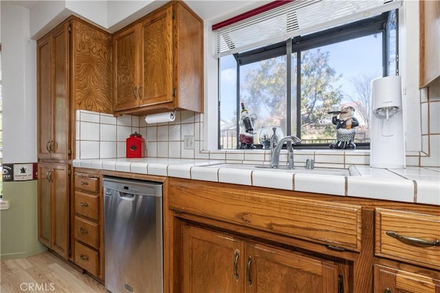 kitchen featuring brown cabinetry, decorative backsplash, light wood finished floors, and stainless steel dishwasher