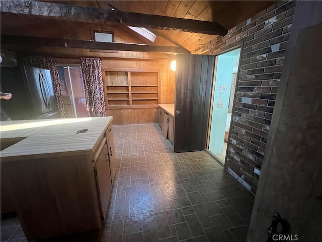 interior space with vaulted ceiling with beams, wooden ceiling, wooden walls, light countertops, and freestanding refrigerator