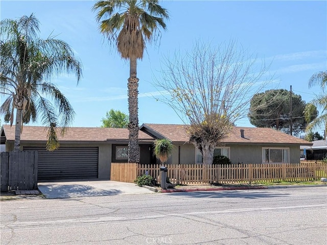 ranch-style home featuring a fenced front yard, concrete driveway, an attached garage, and stucco siding