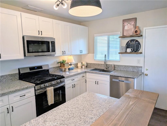 kitchen with open shelves, appliances with stainless steel finishes, a sink, and white cabinetry