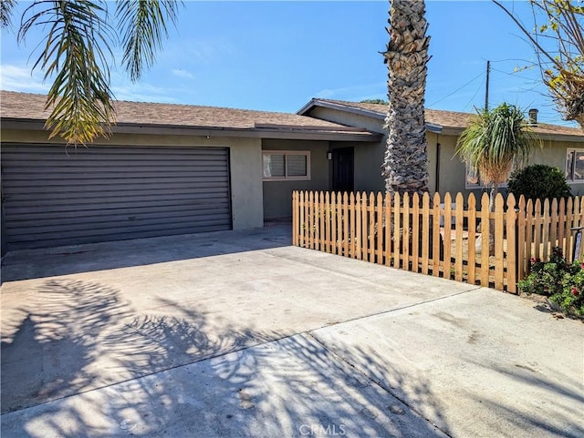 view of front facade with a fenced front yard, concrete driveway, a garage, and stucco siding