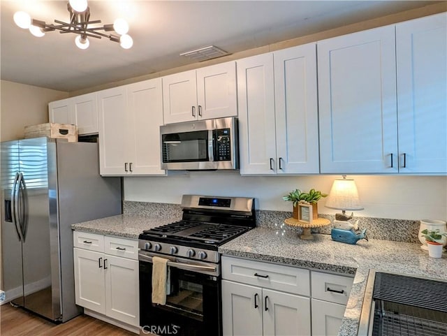 kitchen with a notable chandelier, stainless steel appliances, white cabinetry, light stone countertops, and light wood-type flooring