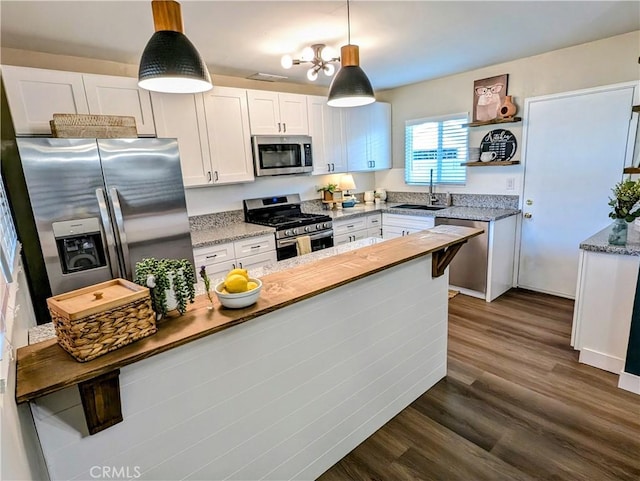 kitchen with white cabinets, appliances with stainless steel finishes, dark wood-style flooring, hanging light fixtures, and a sink