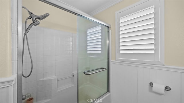 bathroom with combined bath / shower with glass door, wainscoting, and crown molding