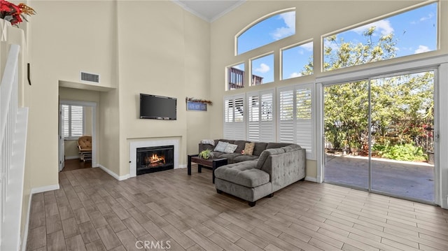 living room with wood finished floors, visible vents, baseboards, a lit fireplace, and crown molding