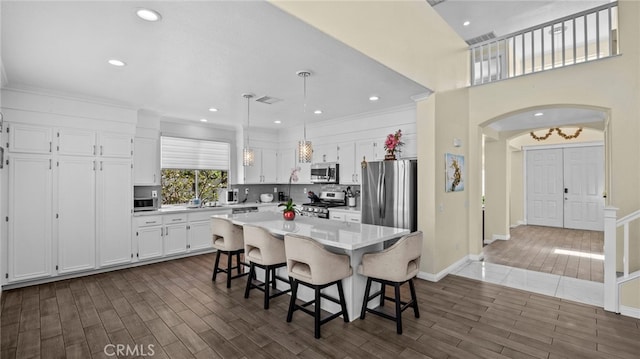 kitchen featuring dark wood-style flooring, light countertops, appliances with stainless steel finishes, white cabinets, and a kitchen breakfast bar