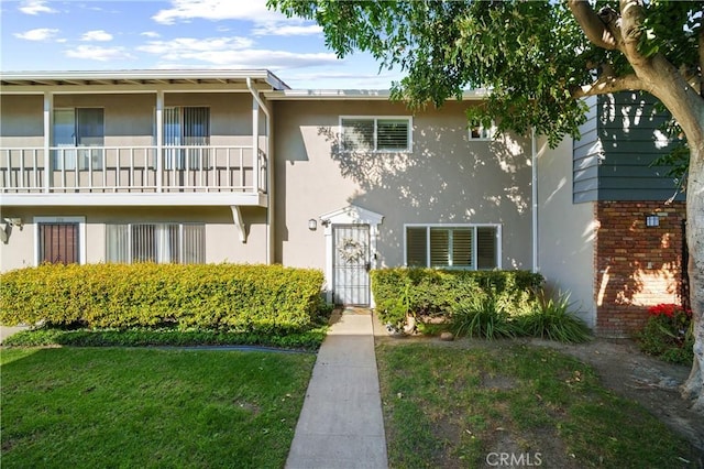 exterior space featuring a front lawn, a balcony, and stucco siding