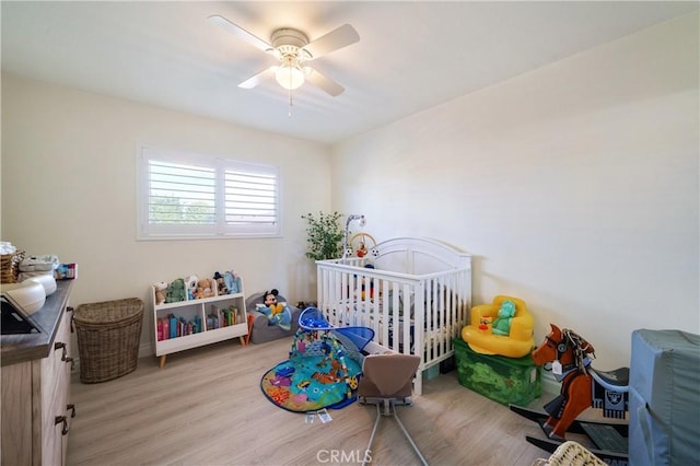 bedroom with a nursery area, ceiling fan, and wood finished floors