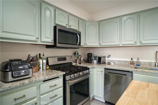 kitchen featuring appliances with stainless steel finishes, a sink, light stone countertops, and green cabinetry