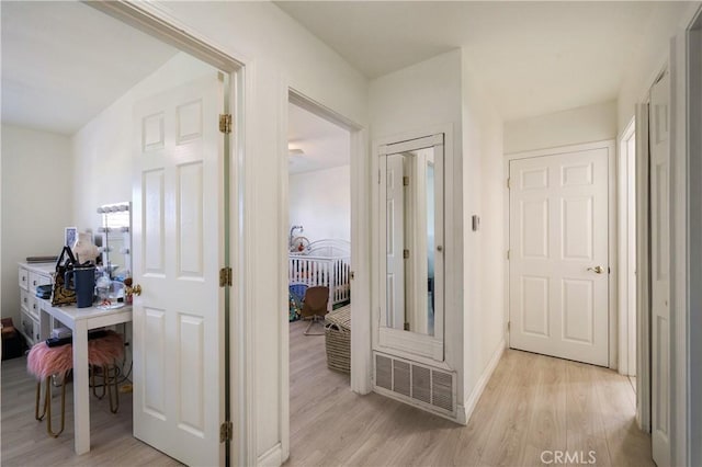 hall with baseboards, visible vents, and light wood finished floors