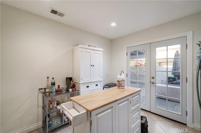 interior space featuring visible vents, white cabinets, wooden counters, french doors, and a center island