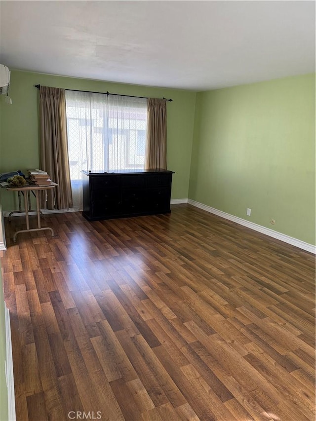 spare room with baseboards, wood finished floors, and a wall mounted AC