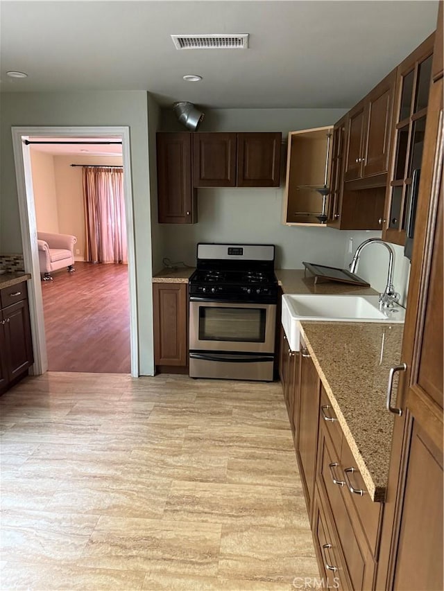 kitchen with light stone counters, visible vents, glass insert cabinets, a sink, and stainless steel gas range