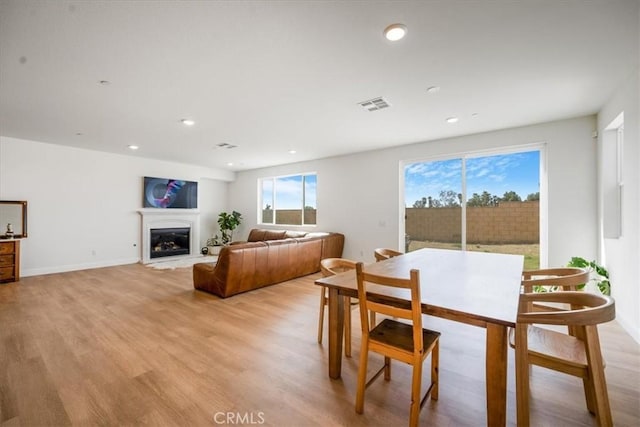 dining area with light wood-style flooring, recessed lighting, visible vents, baseboards, and a glass covered fireplace