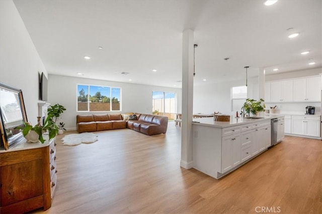 kitchen with light wood finished floors, stainless steel dishwasher, open floor plan, and white cabinetry