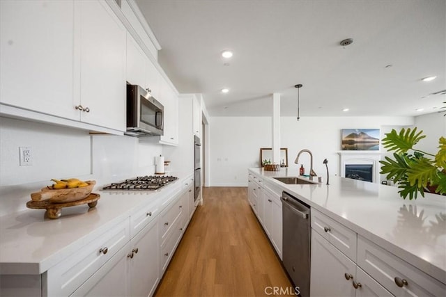 kitchen featuring appliances with stainless steel finishes, light countertops, light wood-type flooring, white cabinetry, and a sink